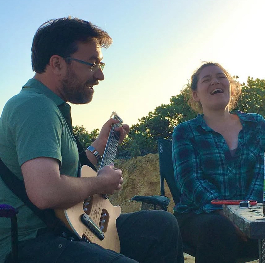 Kevin playing guitar while Meg laughs beside him outdoors